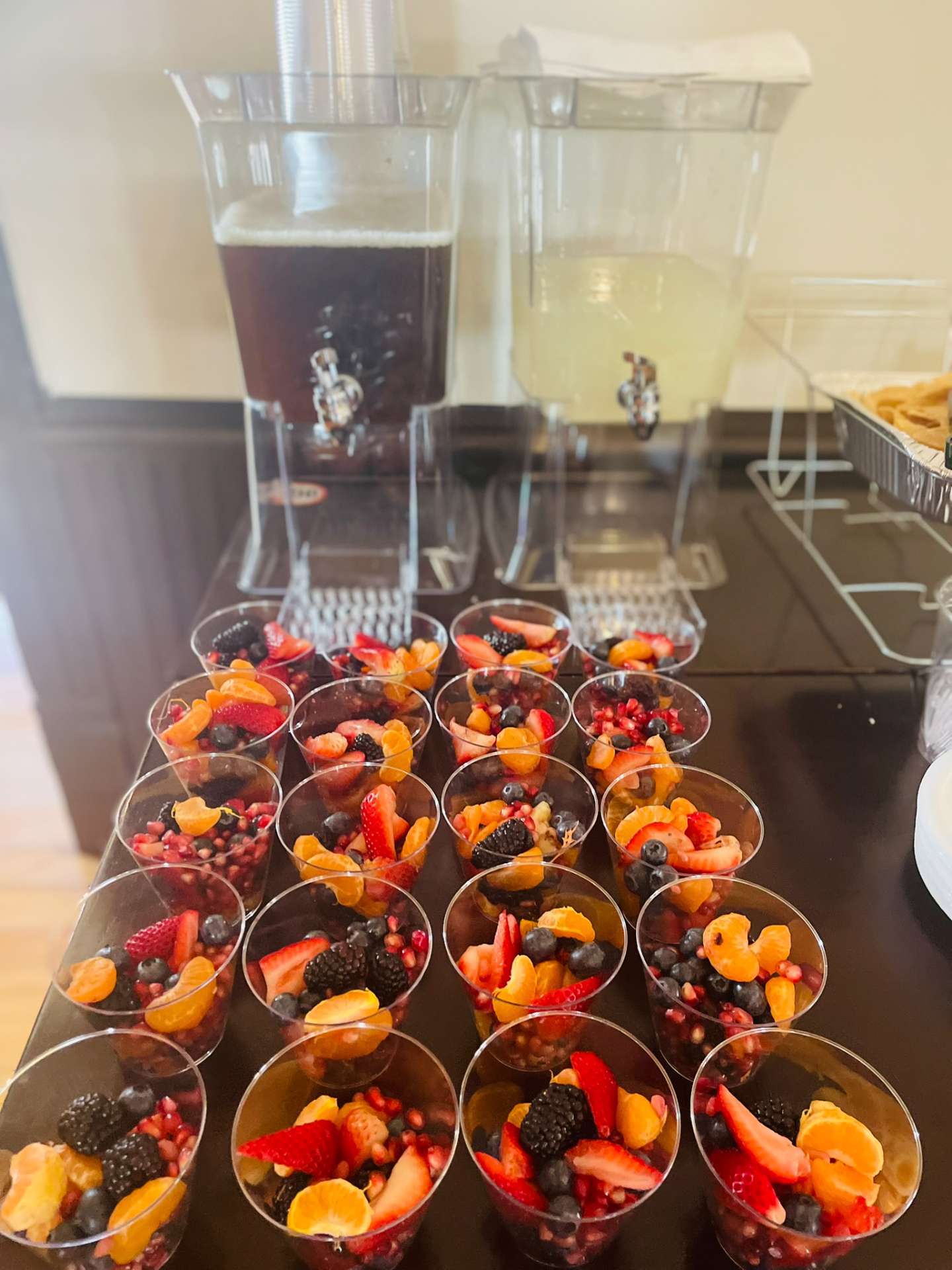 Fresh fruit cups with berries and citrus alongside iced tea and lemonade dispensers for Cafe Mona catering in Stillwater.